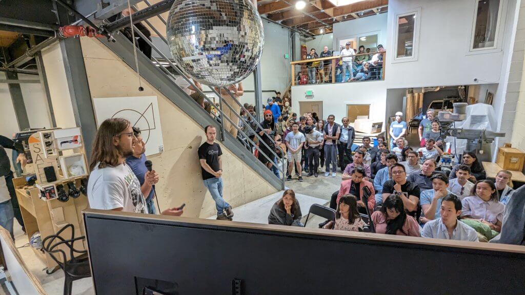 A crowd of participants attentively listen to a speaker at the final awards ceremony.
