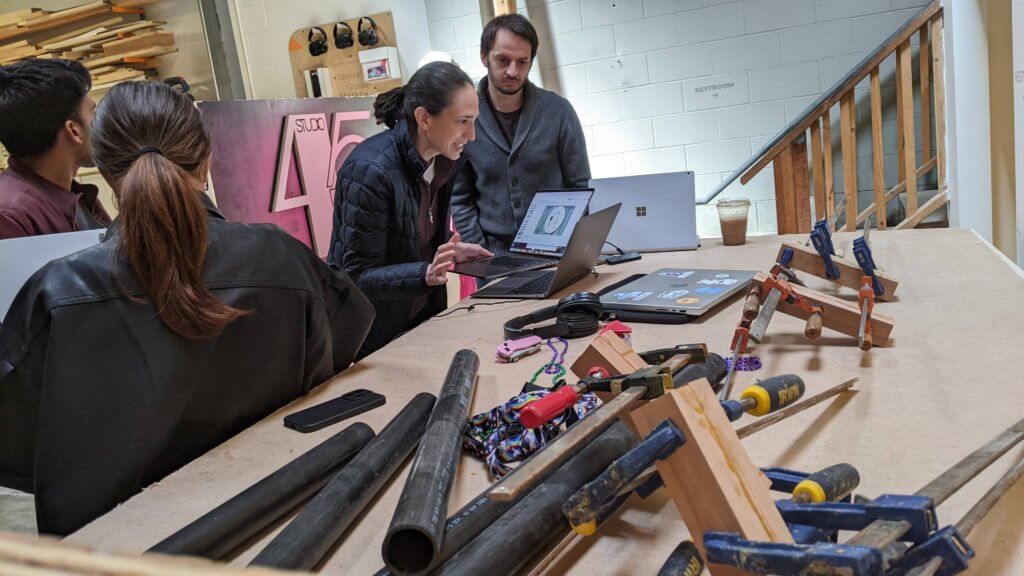 Two team members collaborate at a a table in front of a laptop and an array of materials. 